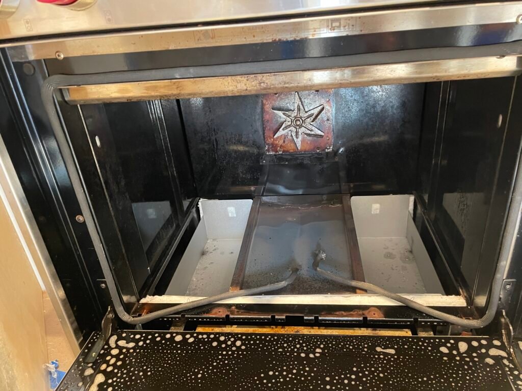 Wolf range showing heating element exposed and gasket replacement in progress, oven door sprayed with degreaser for cleaning