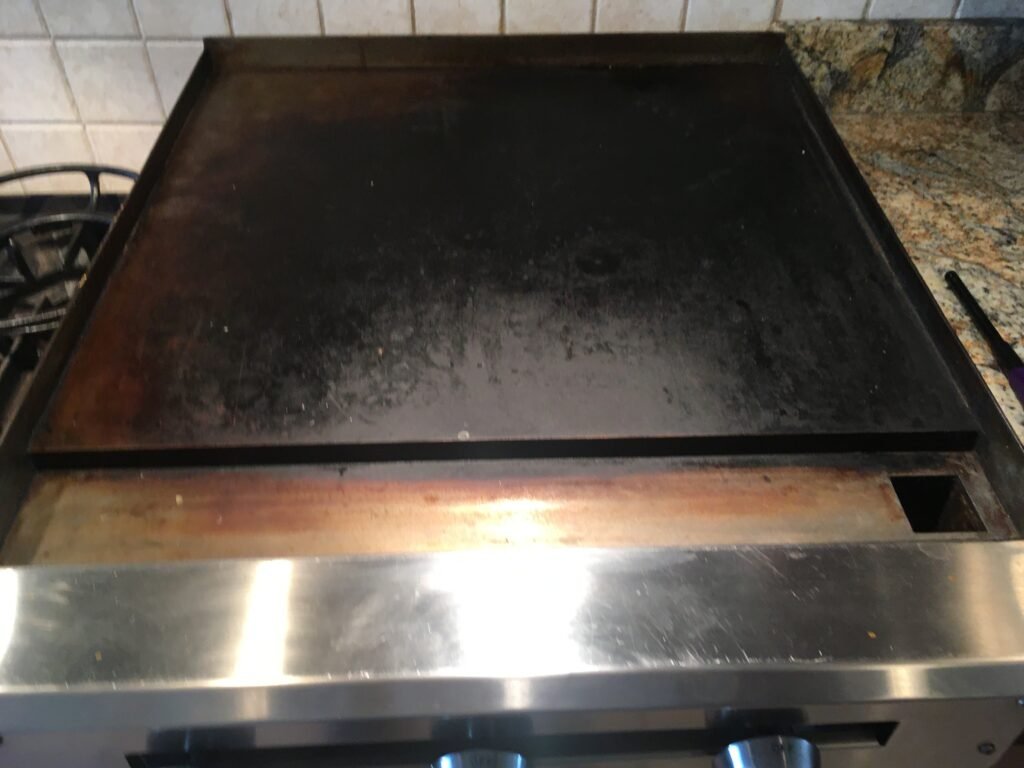 Side‑by‑side comparison of a Vulcan Professional Cooking Range Griddle before professional deep cleaning by OvenPal, showing grease, grime, and residue accumulated on flat top/griddle