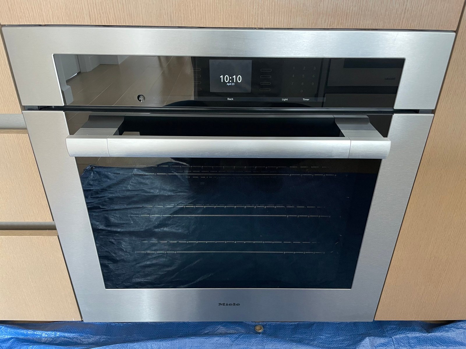 Professional deep cleaning of a Miele built-in electric oven in a New York City luxury kitchen, showing restored glass and polished stainless steel.