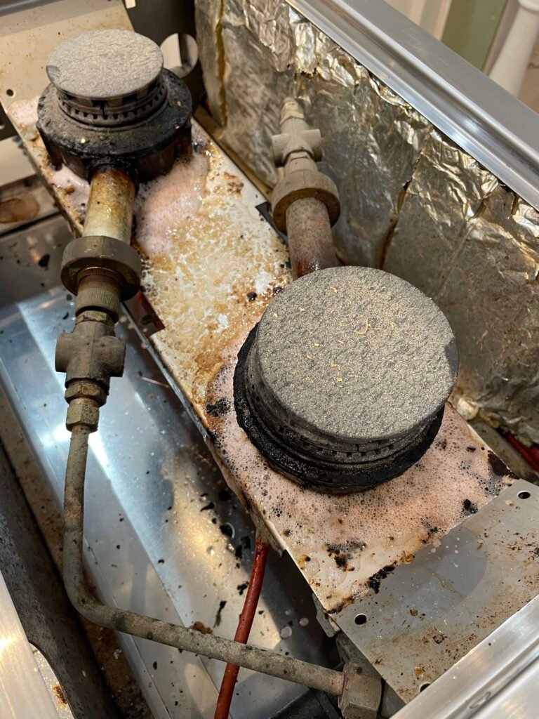 La Cornue brass burners, rings, and caps before range deep cleaning — heavy grease, discoloration, and buildup prior to restoration.