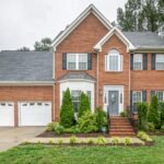 Two‑story brick family house with twin garages and vibrant greenery in Greenwich, Connecticut, representing OvenPal’s expert oven deep cleaning services, professional appliance cleaning, and high‑end kitchen appliance care for Fairfield County residents.