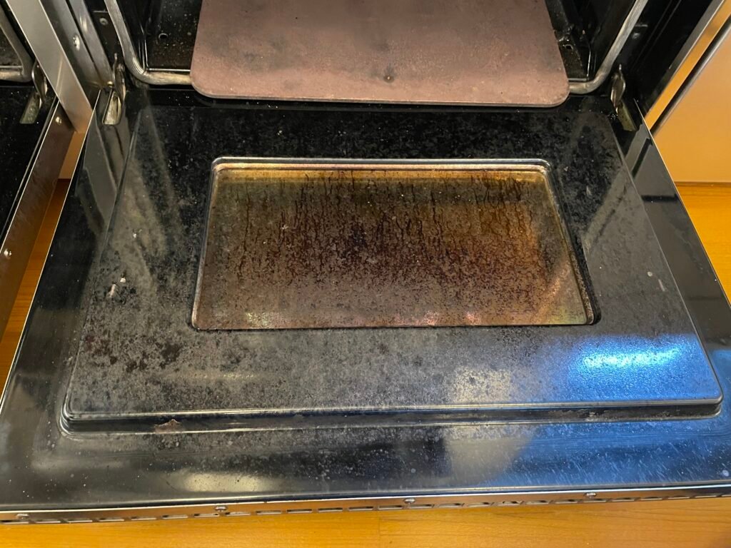 The Wolf range door showed heavy carbon buildup, baked‑on grease, and heat‑stained glass — a common issue in Upper West Side and Chelsea kitchens where high‑heat cooking and limited ventilation trap residue. Carbon around the door frame dulled the stainless steel and reduced visibility inside the oven.