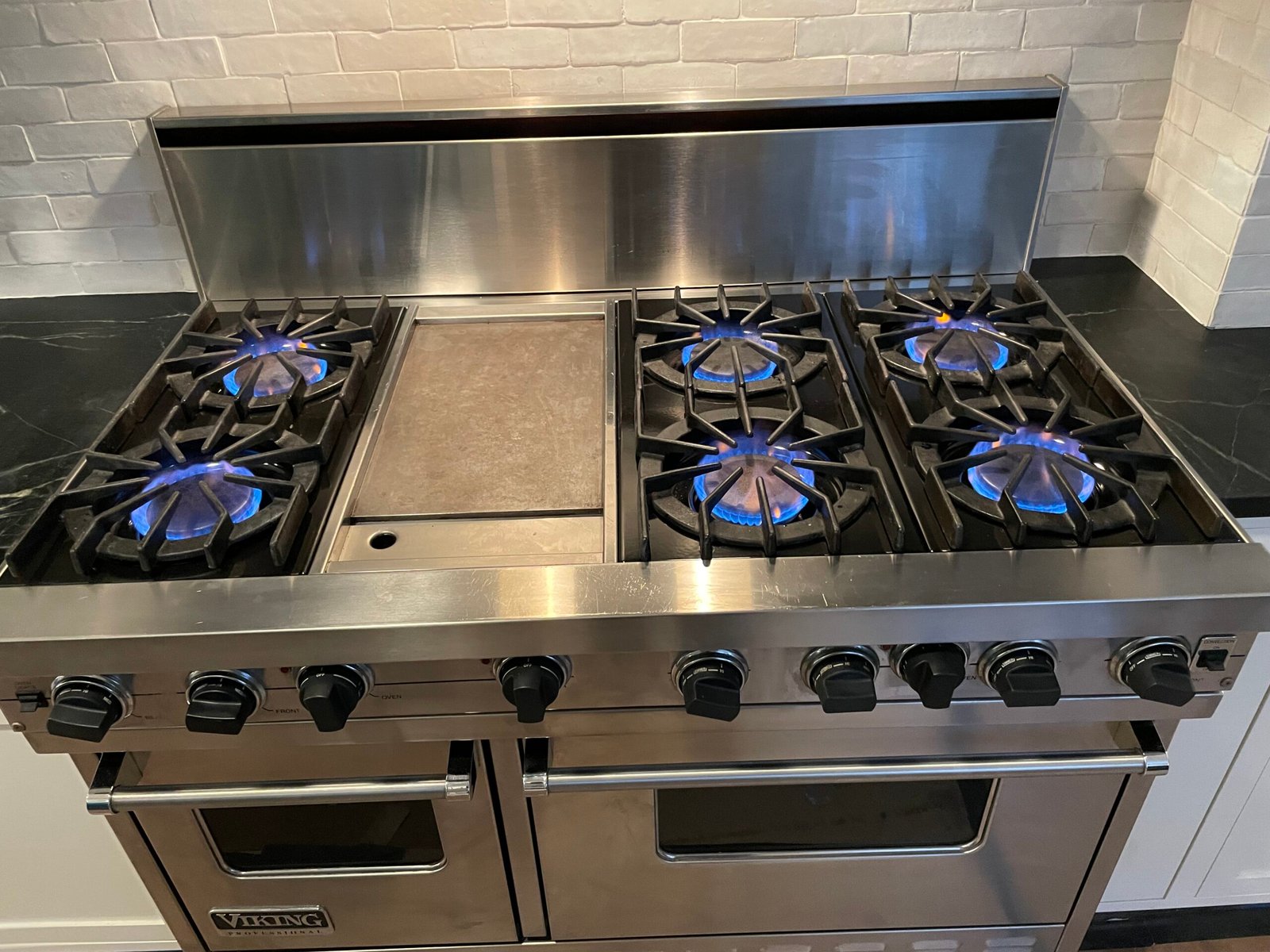 Viking six‑burner gas range with central griddle during a maintenance cleaning in a New York City home, showing burners, control knobs, and stainless‑steel surfaces being degreased.