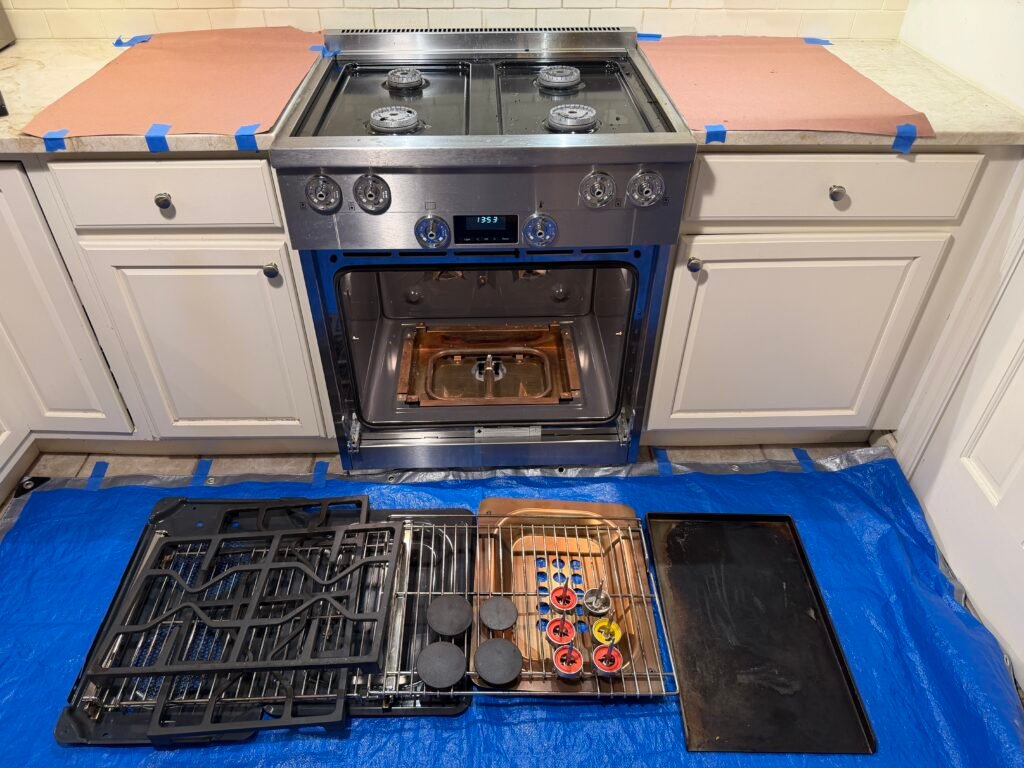 Professional NYC appliance cleaning technician disassembling a Miele gas range by removing interior racks, panels, fan covers, and exterior grates, griddles, knobs, and burner caps for full multi‑appliance service preparation