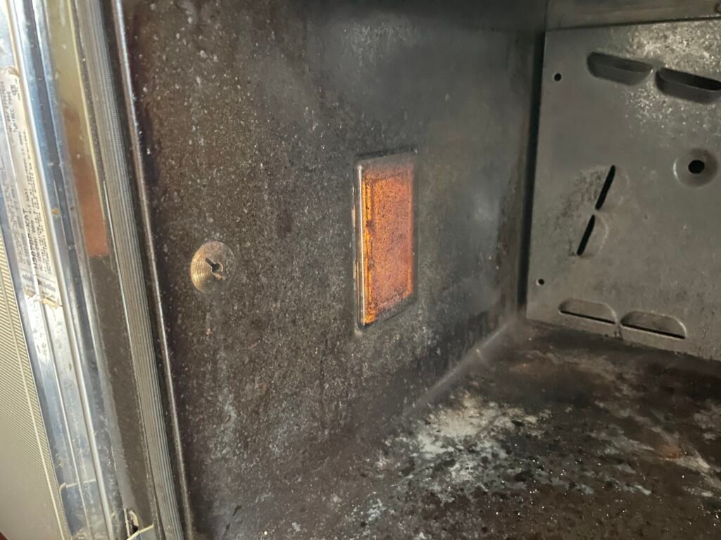 The interior of this Miele gas oven showed heavy grease buildup, darkened rack support posts, residue on the light‑bulb cover, carbon on the vertical rack guides, and a heavily soiled fan‑cover area — common in Upper East Side prewar apartments where ovens run hot and accumulate residue quickly.