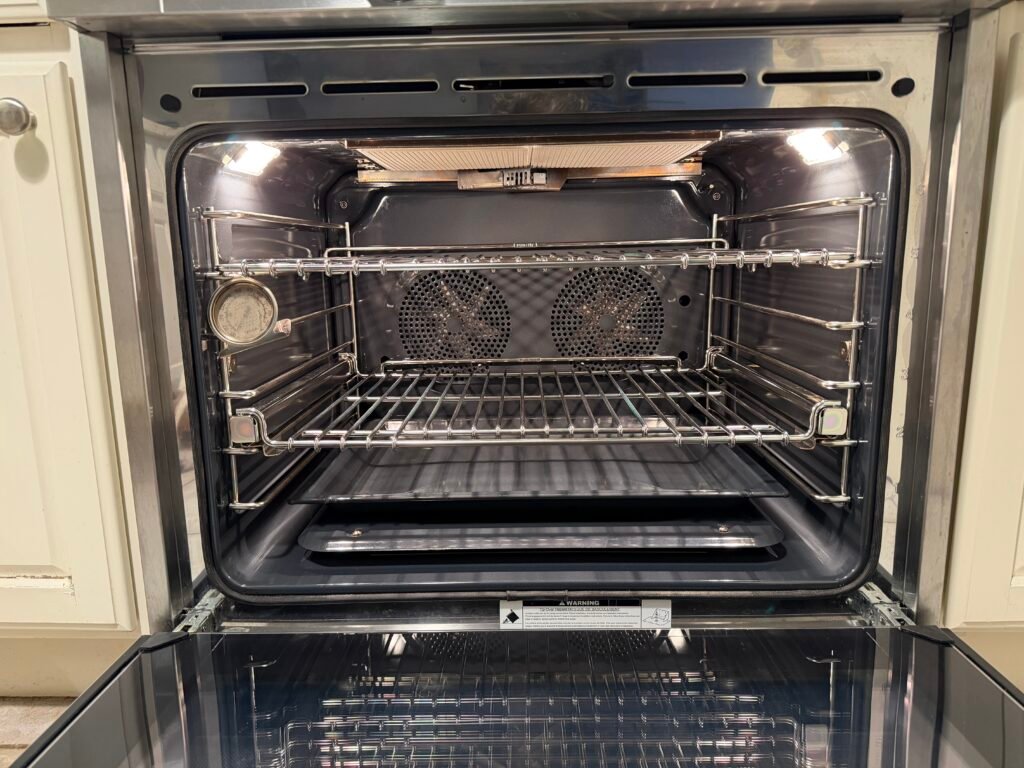 NYC appliance technician performing precision tuning on a Miele gas range, lubricating hinges, optimizing door springs, adjusting gaskets for better heat retention, realigning hardware, replacing bulbs, and securing control knobs